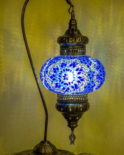 A traditional Turkish-style table lamp with a blue mosaic glass globe and an ornate bronze-colored metal frame, shown illuminated against a warm yellow background.