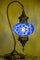 A traditional Turkish-style table lamp with a blue mosaic glass globe and an ornate bronze-colored metal frame, shown illuminated against a warm yellow background.